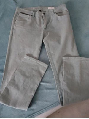 Ljusgrå bootcut jeans från Emilio Denim - Snygga ljusgrå jeans från Emilio Denim med klassisk femficksdesign och bootcut-ben. Byxorna har dragkedja och knapp framtill samt bälteshällor. Materialet är mjukt och slitstarkt jeans, perfekt för dig som gillar en avslappnad stil.Beninnerlängd 78 cm Midja 40