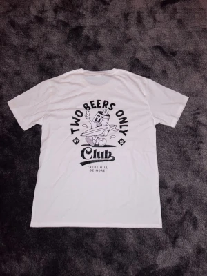 ”Two beers only club (there will be more)” T-shirt - Vit t-shirt med svart tryck och lekfull design. Motivet visar en tecknad ölburk med texten “Two Beers Only Club” samt “There will be more”. En bekväm och stilren tröja med humoristisk känsla – perfekt till vardags.