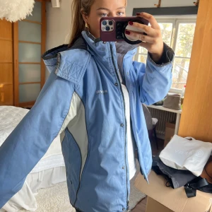 Blå skidjacka  - Säljer en blå skidjacka med dragkedja och knappar. Jackan har en hög krage och justerbar huva. Perfekt för kalla dagar i skidbacken😍😍 