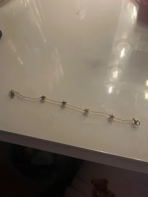 Guldigt armband med stjärnor - Snyggt och tunt armband i guldfärgad metall med fem små stjärnor längs kedjan. Perfekt att kombinera med andra smycken för en cool och personlig stil. Armbandet har ett smidigt lås och passar de flesta handleder.