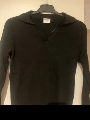 Svart ribbad tröja från & Other Stories - Svart långärmad tröja från & Other Stories i ribbad stickad kvalitet. Tröjan har en klassisk krage och v-ringad hals, vilket ger en snygg och stilren look. Perfekt att matcha med jeans eller kjol för en enkel och cool outfit.