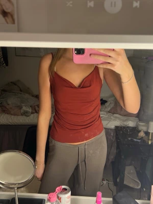 Rostbrun linnetopp med drapering - Säljer en snygg rostbrun linnetopp med smala axelband och draperad halsringning. Toppen har en figurnära passform och är perfekt för dig som gillar stilrena och enkla plagg med lite extra detalj. Materialet känns mjukt och lätt mot huden.