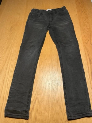 Levi's 512 Slim Taper jeans pris kan diskuteras  - Svarta Levi's 512 Slim Taper jeans med klassisk femficksdesign och smal, avsmalnande passform. Jeansen har metallknappar, bälteshällor och den ikoniska röda Levi's-taggen på bakfickan. Materialet är mjukt och stretchigt denim för extra komfort.