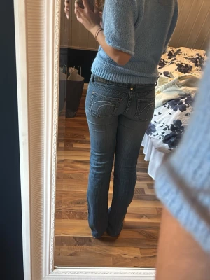 Blå low waisted bootcut jeans, second hand  - Säljer ett par snygga blå jeans från secondhand butik med bootcut-snitt och klassiska detaljer på bakfickorna. Jeansen har normal passform och är tillverkade i jeansmaterial med en mörkare tvätt. Perfekta för dig som gillar en tidlös stil. Ny tvättade är midjemåttet ca 38 cm men de stretchas ut efter användning.