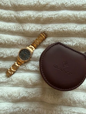 Guldfärgad klocka  - Elegant guldfärgad klocka från Dyrberg/Kern med diamantdetaljer. Tidlös design som kombinerar lyx och vardagsfunktion, perfekt både till vardag och fest. 	•	Guldfärgat rostfritt stål 	•	Diskreta diamantdetaljer som ger en sofistikerad look 	•	Vattentålig 	•	Levereras i GANT-klockask 	•	Passar mindre handled, ca 16 cm  En stilren accessoar för dig som vill ha något klassiskt, feminint och hållbart över tid. 