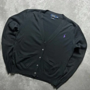 Svart cardigan från Polo Ralph Lauren  - Svart cardigan från Polo Ralph Lauren i 100% pimabomull. Tröjan är i nyskick och endast använd ett fåtal gånger. Nypris ca 2400kr mitt pris endast 349kr. Tröjan är VÄLDIGT limiterad second hand så först till kvarn! Klassisk v-ringad modell med lila broderad logga på bröstet, knappar framtill och två fickor. Perfekt för dig som gillar stilrena och tidlösa plagg. Vid frågor eller funderingar är det bara att säga till Mvh. 