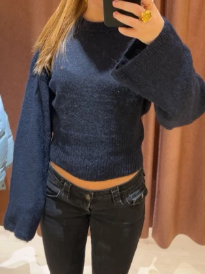 Mörkblå stickad tröja - Säljer en mörkblå croppad stickad tröja från Gina Tricot  med breda, långa ärmar och rund hals. Tröjan har en mjuk och fluffig känsla, perfekt för att ge en chill vibe till din outfit. Passar dig som gillar en loose fit och vill ha något enkelt men ändå snyggt. Använd få gånger.