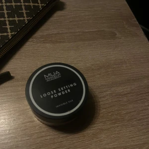MUA Loose Setting Powder Invisible Silk - Transparant löspuder från MUA Makeup Academy i färgen Invisible Silk. Kommer i en rund plastburk med svart lock och sifter för enkel applicering. Perfekt för att fixera din bas och ge en matt finish utan att kännas tung.