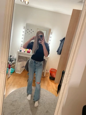 Ljusblå bootcut jeans med slitning - Säljer ett par ljusblå jeans med bootcut-modell och slitning vid knäet. Jeansen har klassisk femficksdesign, låg midja och är tillverkade i jeansmaterial.