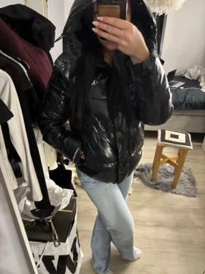 Svart glansig pufferjacka med huva - Snygg svart pufferjacka med glansig finish och stor huva. Jackan har dragkedja framtill och sidofickor, perfekt för kalla dagar. Passar dig som vill ha en trendig och bekväm look. Pris går att diskutera🫶🏼