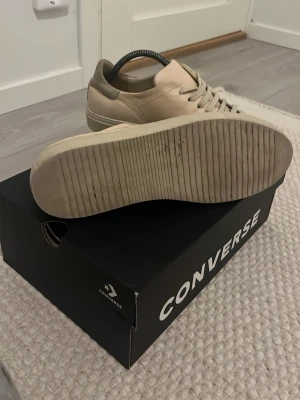 Beige sneakers från Axel Arigato - Stilrena beige sneakers från Axel Arigato med rund tå och platt sula. Skorna har snörning och är tillverkade i slätt skinn med diskret logga på sidan. Perfekta för en clean och modern look.