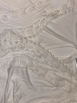 Vit kort klänning med spetsdetaljer - Romantisk vit kort klänning med vackra spetsdetaljer och broderade band över bröstet och midjan. Klänningen har en luftig passform och långa ärmar med spetskant. Perfekt för sommarens alla tillfällen.