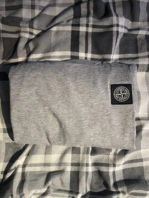 Grå Stone Island t-shirt i bomull - Säljer en stilren grå t-shirt från Stone Island med klassisk logopatch på bröstet. T-shirten har rund hals och är tillverkad i mjuk bomull för skön känsla. Perfekt till jeans eller shorts för en clean look.