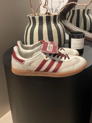 Adidas Samba OG vit/röd sneakers - Snygga Adidas Samba OG sneakers i vitt och rött med klassiska tre ränder på sidan. Ovandel i skinn och mocka, detaljer i rött och vit sula. Perfekta för dig som gillar retrostil och streetwear. Skorna har snörning och en platt gummisula. Skriv vid frågor eller skicka prisförslag!✅💸