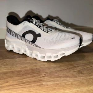 Oanvända On oncludmaster2 Running sneakers  - Snygga vita sneakers från On Running med svart logga och text på sidan. Skorna har en futuristisk, ventilerad ovandel och en unik, chunky sula med hålrum för extra komfort. Svarta och vita detaljer, snörning och låg profil. Perfekta för dig som gillar sportig stil.
