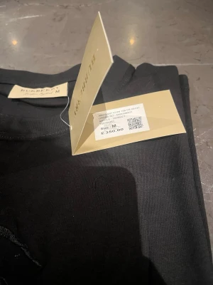 Svart Burberry t-shirt och Ralph T-shirt  - 2x bundleSnygg svart t-shirt från Burberry med diskret broderad logga och motiv på bröstet. Klassisk passform och rund halsringning. Tillverkad i mjuk bomull som känns skön mot huden. Perfekt för dig som vill ha en stilren och exklusiv look.