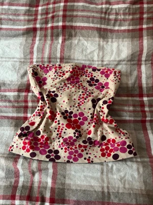 Prickig tubtopp 🩷 - Säljer en tubtopp från H&M i beige med färgglada prickar i rosa, lila och rött. Toppen är axelbandslös och har en bandeau-form som sitter snyggt på kroppen. Perfekt för varma dagar och enkel att styla med jeans eller kjol.💕💕