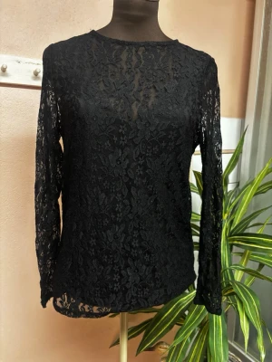 Svart spetsblus med lång ärm - Säljer en svart blus i genombruten spets med blommigt mönster. Blusen har lång ärm och rund halsringning. Perfekt för dig som vill ha en elegant och trendig topp med transparent känsla.