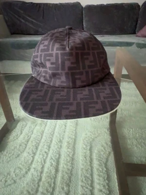 Brun Fendi keps med FF-mönster - Säljer en brun keps från Fendi med det klassiska FF-logomönstret över hela kepsen. Kepsen har böjd skärm och justerbart band bak för perfekt passform. Materialet är slitstarkt tyg som känns lyxigt och trendigt.