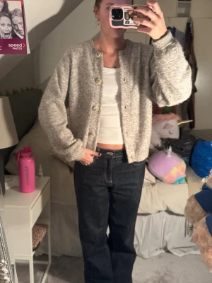 Grå stickad kofta med knappar - Mysig grå stickad kofta med rund halsringning och stora knappar framtill. Koftan har en rak, lite boxig passform och är perfekt att slänga över en t-shirt eller linne. Passar dig som gillar en enkel och stilren look.