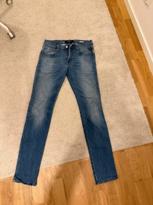 Replay Anbass blå jeans herr - Snygga blå Replay Anbass jeans med klassisk femficksdesign och raka ben. Jeansen har en lätt tvättad look med subtila slitningar och är tillverkade i mjuk bomullsdenim. Perfekta för dig som gillar en stilren och modern passform.