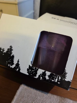 Dricksglas - Välkända SEA Glasbruk (Kosta, Sweden). Glasen har en modern design med en rustik touch och kommer i den snygga originalförpackningen med klassiskt skogsmotiv.  ​Dessa passar perfekt som stämningsfulla ljuslyktor eller som rustika glas för servering. En utmärkt present till någon som uppskattar svensk glaskonst!  ​Märke: SEA Glasbruk, Kosta Sweden.  ​Färger: En i en djup lila/burgundy ton och en i rökigt grått/svart.  ​Skick: Helt nya och oanvända i originalförpackning