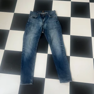 Lee Jeans - Klassiska blå Lee Austin jeans med straight fit och normal passform. Jeansen har fem fickor, knappgylf och subtila slitningar för en avslappnad look. Tillverkade i tåligt denimtyg av bomull. Perfekta till vardags för en stilren och enkel outfit. Storlek W 30 L 34