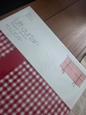 Röd hissgardin KULLTORP med hjärtan - Säljer en röd och vit hissgardin från KULLTORP med rutigt mönster och dekorativa hjärtan samt spetskant. Gardinen har klassisk lantlig stil och är tillverkad i tyg. Perfekt för att skapa en mysig känsla i köket eller vardagsrummet.