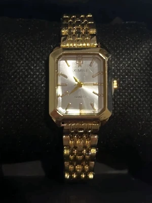 Guldfärgad fyrkantig klocka Ximili - Stilren klocka från Ximili med fyrkantig urtavla i silver och guldfärgat armband i metall. Klockan har en klassisk länkdesign och tydliga markeringar på urtavlan. Perfekt accessoar för dig som gillar en elegant och modern look.