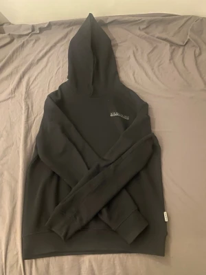 Svart hoodie från Napapijri - Snygg svart hoodie från Napapijri med diskret logga på bröstet och en större, vågig logga på ryggen. Klassisk passform med huva och ribbade muddar. Perfekt för dig som gillar streetwear och vill ha något stilrent. Materialet känns mjukt och bekvämt.  Nästan helt ny använd typ 6 ggr. 