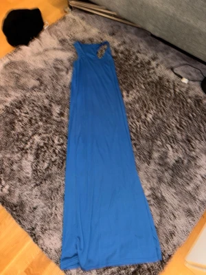 Blå långklänning med brottarrygg - En stilren blå långklänning med brottarrygg och ärmlös design. Klänningen har en enkel, rak passform och är tillverkad i ett mjukt, stretchigt material som känns bekvämt mot huden. Perfekt för dig som gillar minimalistisk stil.