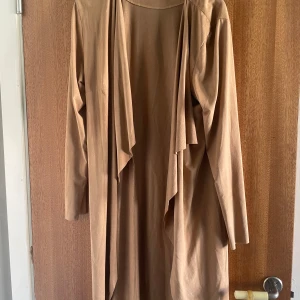 Beige trenchcoat från NLY Trend - Snygg beige trenchcoat från NLY Trend i mjukt material. Jackan har långa ärmar, öppen front med draperad krage och hällor för bälte i midjan. Perfekt för lager-på-lager och en clean look.