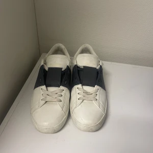 Valentino Garavani vita sneaker - Säljer ett par vita Valentino Garavani sneakers med mörkblå band över vristen. Kommer med dustbag och påse. Perfekta för dig som gillar stilrena och exklusiva sneakers. Hör av dig vid funderingar