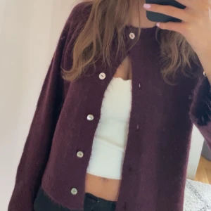 Vinröd kofta med knappar - Mysig vinröd kofta med stora silvriga knappar framtill. Koftan har en rak, lite loose passform och är stickad i ett mjukt material. Perfekt att slänga över en topp för en chill look. Aldrig använt 