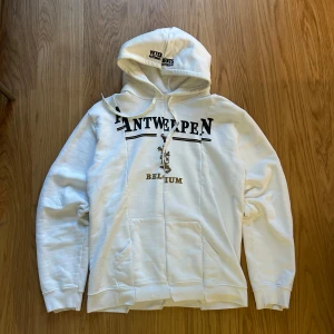 Vetements Antwerpen hoodie - Vit hoodie från Vetements med tryck 'Antwerpen Belgium' och ett lejon på bröstet. snörning i huvan och ribbade muddar. Perfekt för dig som gillar streetwear och vill sticka ut med en clean look. (Not authentic)