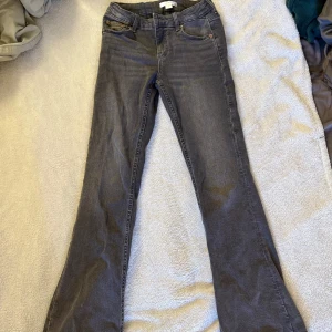 Grå bootcut jeans från Gina Tricot - Snygga grå jeans från Gina Tricot i storlek 146. Modellen har bootcut-ben och klassisk femficksdesign. Jeansen är i mjukt denimtyg och har justerbar midja med knappresår för perfekt passform.