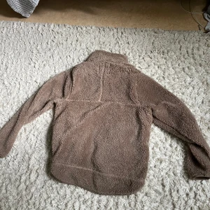 Brun teddyjacka med dragkedja - Mysig brun teddyjacka med hög krage och hel dragkedja framtill. Jackan har lång ärm och är tillverkad i fluffigt teddy-material som ger en skön och avslappnad look. Perfekt för kyliga dagar när du vill vara både varm och snygg.