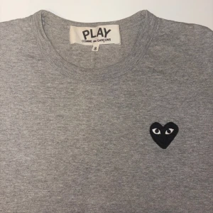Grå t-shirt Comme des Garçons Play - Grå t-shirt från Comme des Garçons Play med det ikoniska svarta hjärtat med ögon broderat på bröstet. Köptes på NK för några år sedan och har inte använts mycket då jag växt ur den.