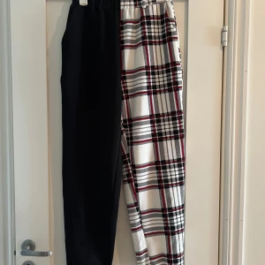 Svart och rutig byxa från SHEIN XS - Unika byxor från SHEIN i storlek XS med ena benet helsvart och andra benet i vitt rutigt mönster med röda och svarta detaljer. Byxorna har resår i midjan och är tillverkade i ett mjukt, bekvämt material. Perfekt för dig som vill sticka ut med din stil.