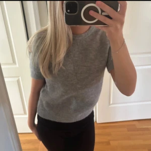Grå stickad kortärmad tröja - Mysig grå stickad tröja med korta ärmar och rund halsringning. Perfekt för lager-på-lager och passar till både jeans och kjol. Enkel och stilren design som funkar året runt.