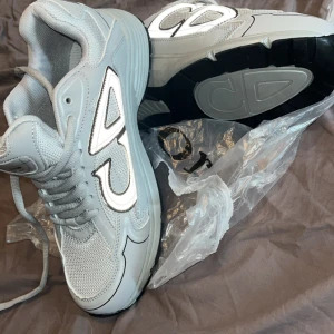 Grå sneakers helt nya - Snygga grå sneakers. Skorna har en chunky sula, mesh och syntetpaneler samt snörning framtill. Insidan är vadderad för extra komfort och sulan är svart undertill. Perfekta för dig som gillar exklusiv streetstyle.