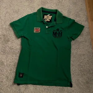 Grön pikétröja från Morris - Snygg grön pikétröja från Morris med klassisk krage, korta ärmar och broderad logga på bröstet. Perfekt för en stilren look.