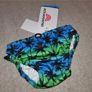 Badbyxor  - Coola badbyxor från Aquarapid i blått och grönt med svart palmtryck. Resår i midja och ben för skön passform. Tillverkade i 100% polyester, perfekta för strand eller pool. Märket syns tydligt baktill.