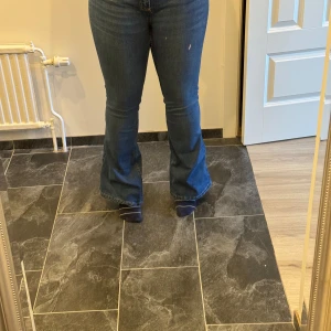 Blå bootcut jeans med hög midja - Snygga blå jeans med bootcut-modell och hög midja. Jeansen har klassisk femficksdesign och är tillverkade i stretchigt denimtyg för en bekväm passform. Perfekta för dig som gillar en tidlös och trendig look.