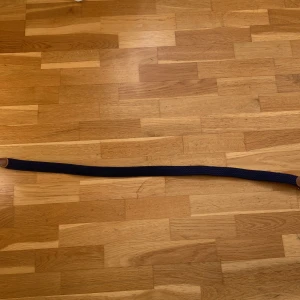 Mörkblå flätat bälte med skinn - Snyggt mörkblått flätat bälte med bruna skinn-detaljer och silvrigt spänne. Bältet har en stilren design med kontrastsömmar på skinnet och passar perfekt till jeans eller chinos. Materialet är mjukt och flexibelt, vilket gör det bekvämt att bära hela dagen.