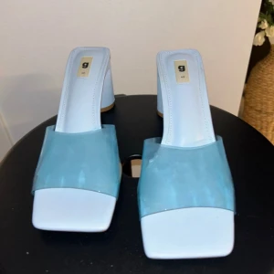 Blåa klackade sandaler med transparent rem - Snygga ljusblå sandaler med bred transparent rem över foten och fyrkantig tå. Skorna har en stabil blockklack och platt sula framtill. Perfekta för dig som vill sticka ut med en modern och fräsch look. Materialet är syntet och designen är riktigt trendig. Skorna är aldrig använda därav topp skick. True to size. Ny pris: 499kr