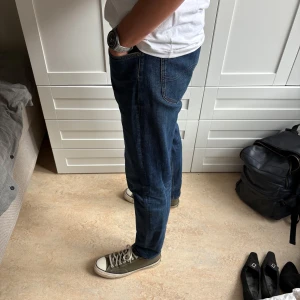 Mörkblå jeans från Lee - Säljer ett par mörkblå jeans från Lee med klassisk femficksdesign och snygga kontrastsömmar. Jeansen har normal passform och raka ben, tillverkade i slitstarkt denimtyg. Perfekta för dig som gillar en tidlös och clean look. Size W33 L34 (jag på bilden är 190cm och väger 78 kg)