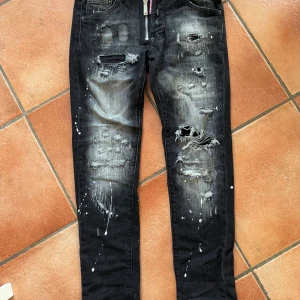 Svarta skinny jeans från Dsquared2 - Snygga svarta jeans från Dsquared2 med slitningar, hål och coola färgstänk. Jeansen har dragkedja framtill med Dsquared2-logga. Storlek S