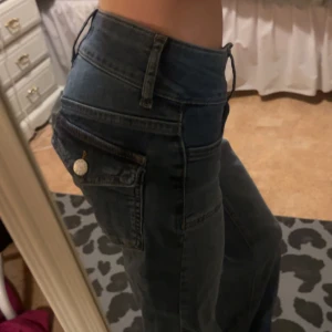 Blå bootcut jeans med låg midja - Säljer ett par blå jeans med låg midja och bootcut-ben. Jeansen har coola fickdetaljer med knapp på sidan och klassiska bälteshällor. Materialet är jeans och passformen är normal. Perfekta för dig som gillar retrovibbar och snygg siluett.