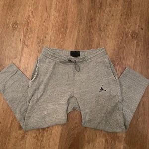 Grå Jordan mjukisbyxor med snörning - Grå mjukisbyxor från Jordan med klassisk Jumpman-logga broderad i svart på benet. Byxorna har snörning i midjan och två sidofickor. Tillverkade i mjukt bomullsmaterial för maximal komfort och avslappnad stil.